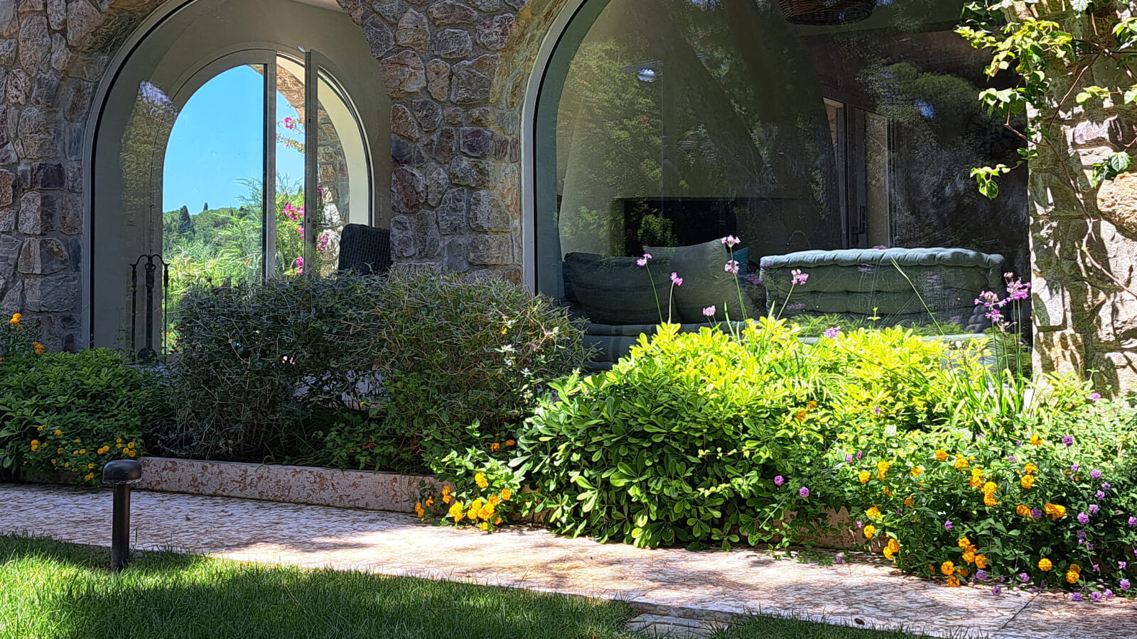 Facciata in pietra con aiuole fiorite e percorso esterno, intervento di landscape design